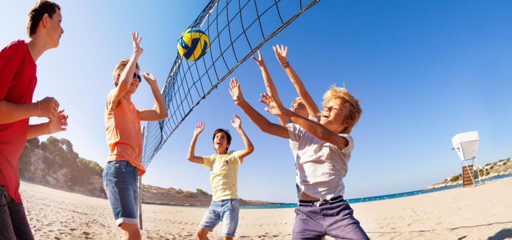 Beachcamps im Jugend-Reisebüro - Jugendliche spielen Volleyball an einem sonnigen Strand unter einem weiten blauen Himmel.