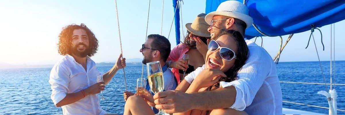 Gruppe junger Menschen auf einem Segelboot beim Anstoßen mit Sekt unter blauem Himmel – Gruppenreise mit JUREBU